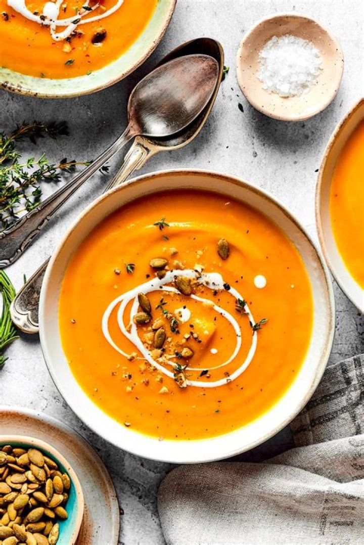Butternut squash soup in two white bowls topped with pumpkin seeds.