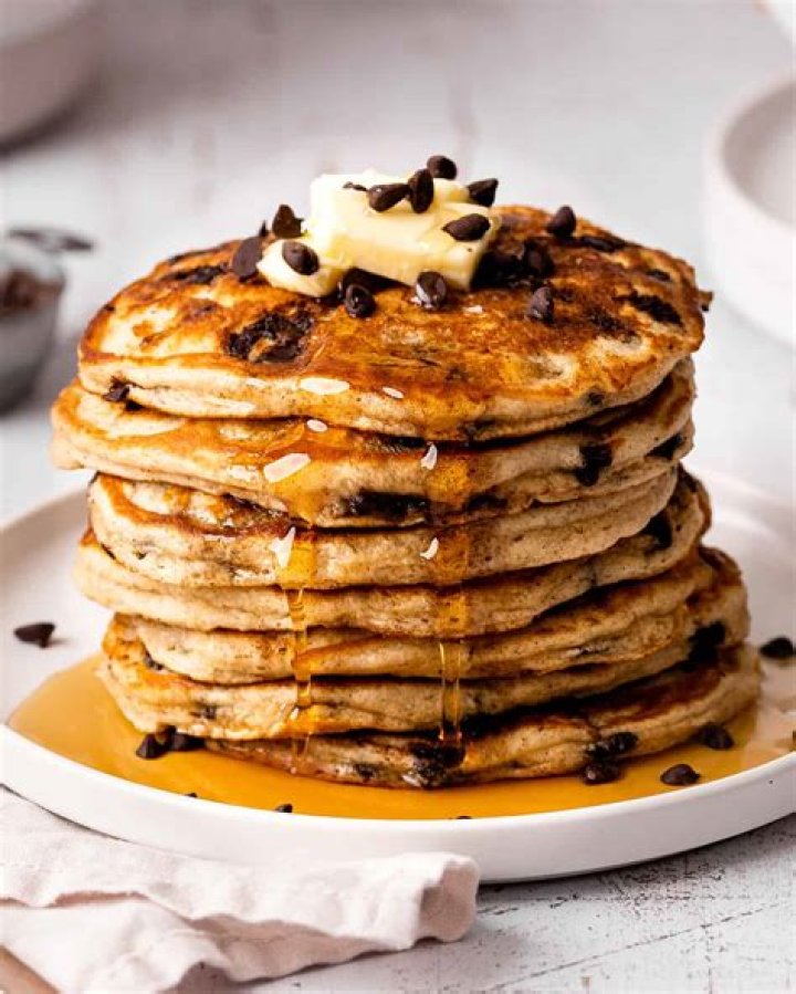 Stack of chocolate chip pancakes covered in strawberry syrup.
